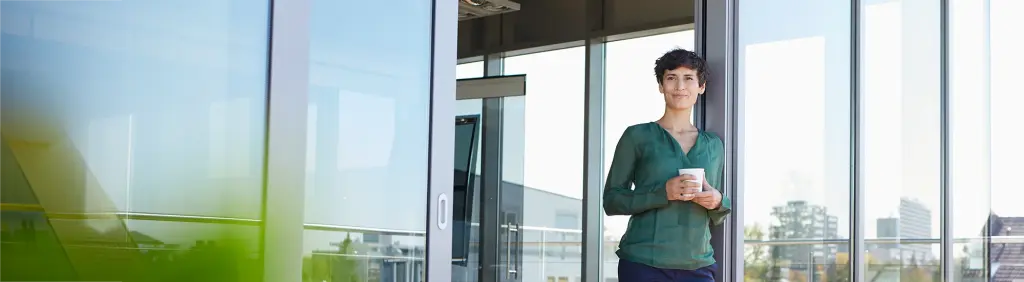 Frau steht mit Kaffee auf der Terrasse